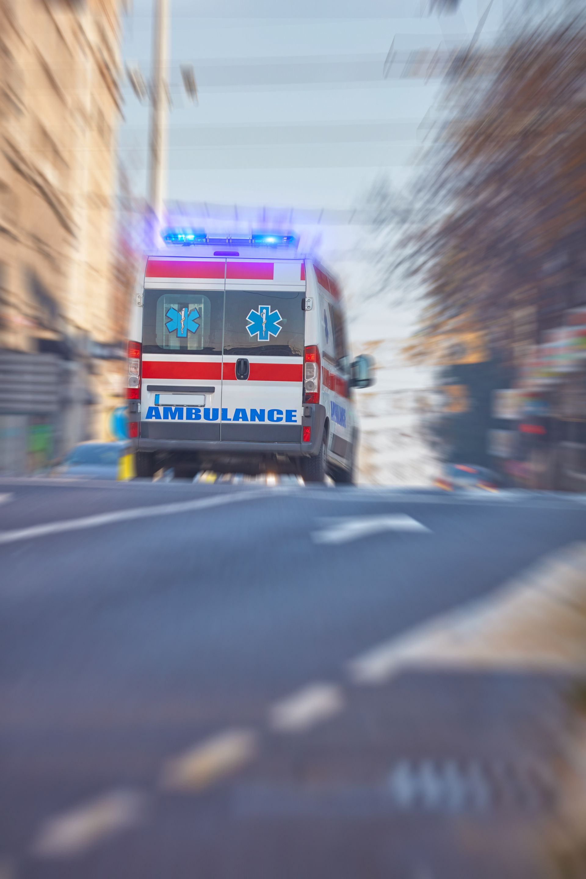 Ambulance roulant à toute vitesse dans la rue, lumières bleues clignotantes, arrière-plan flou.