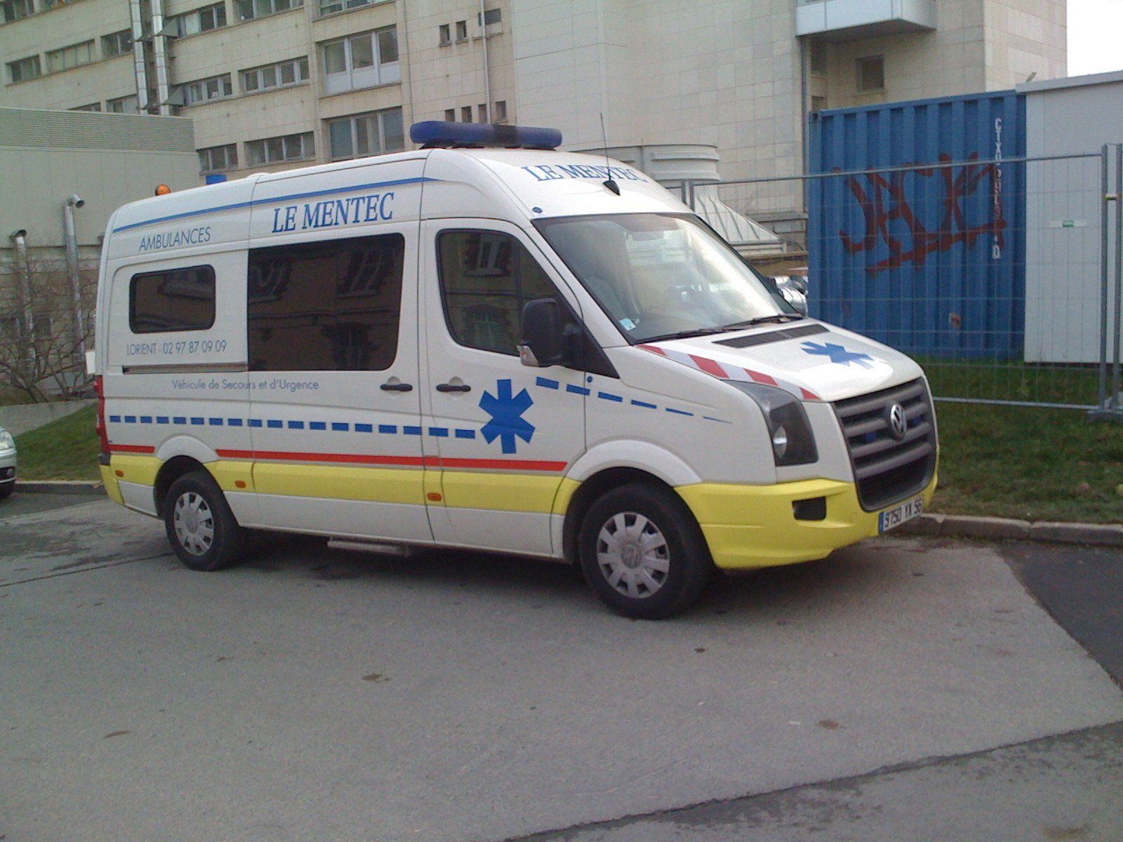 Ambulance blanc et jaune avec symbole d'étoile bleue, garée près d'un bâtiment.