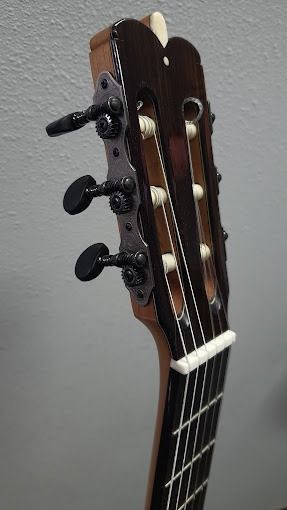 Un primer plano del clavijero de una guitarra acústica contra una pared blanca.