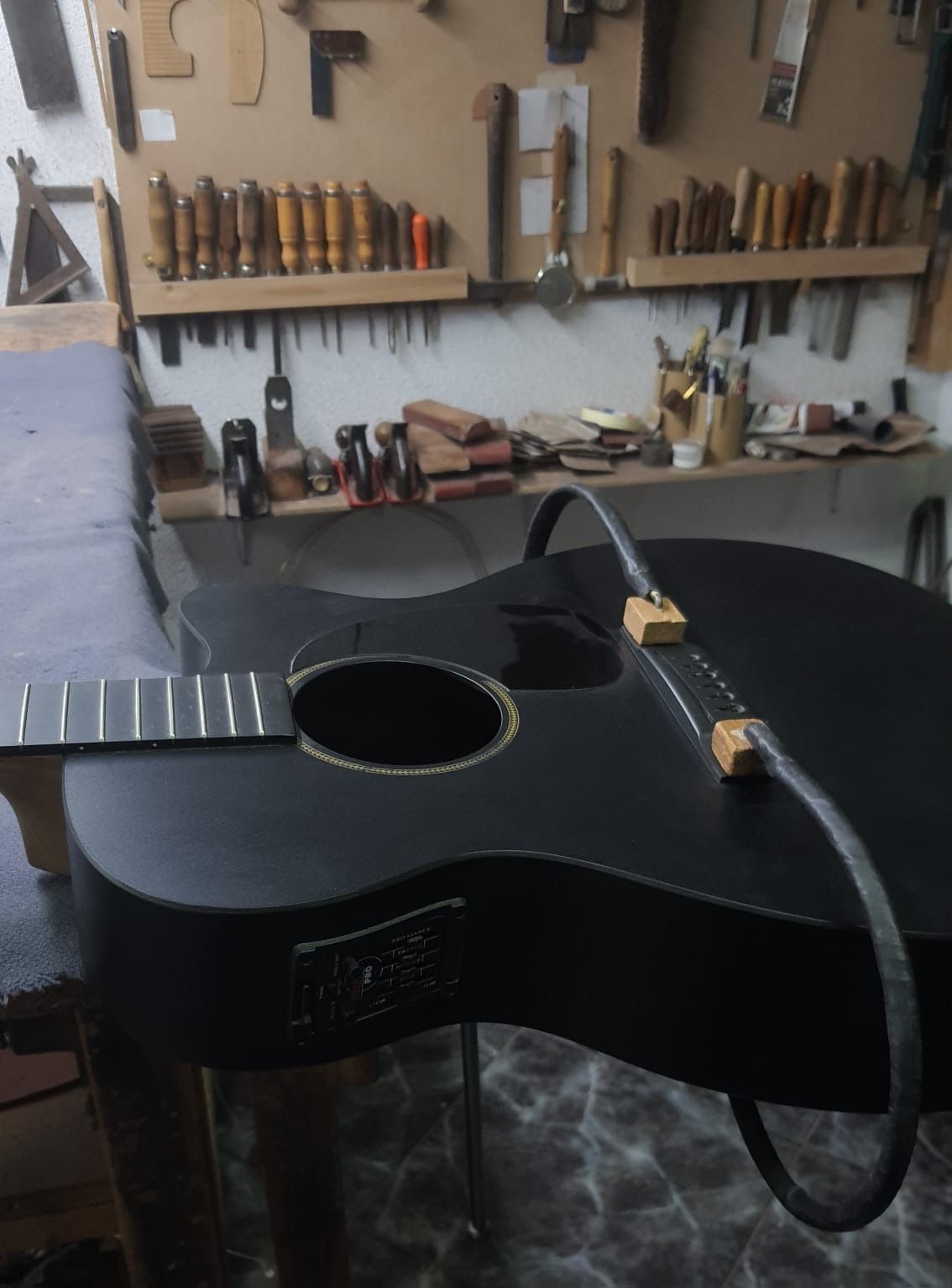 Una guitarra negra está sobre una mesa en un taller.