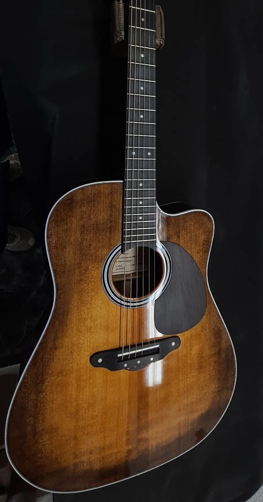 Una guitarra acústica está colgada en una pared negra.