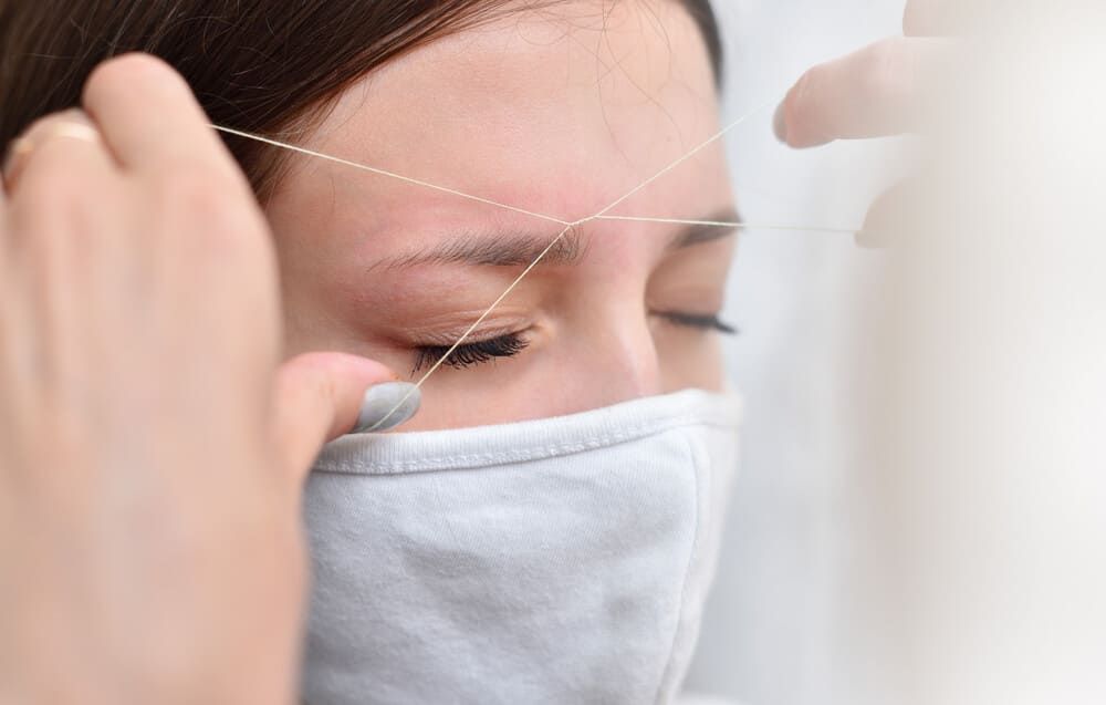 Una mujer que lleva una máscara se está depilando las cejas.