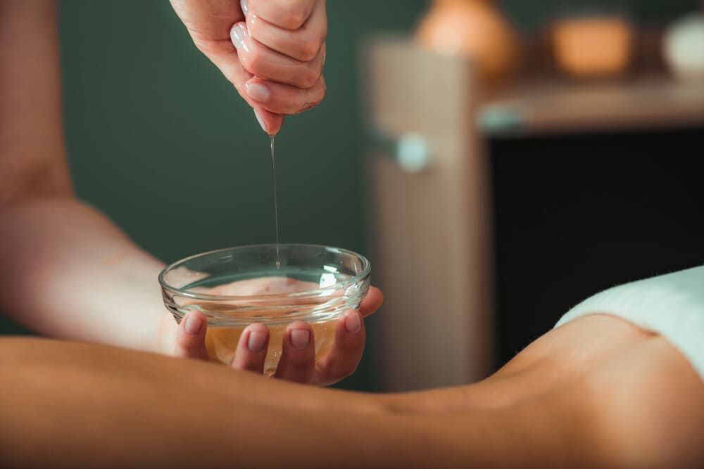 Una persona está vertiendo aceite en un recipiente en el brazo de una mujer.