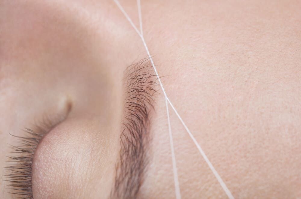 Un primer plano de las cejas de una mujer siendo enhebradas con un hilo.