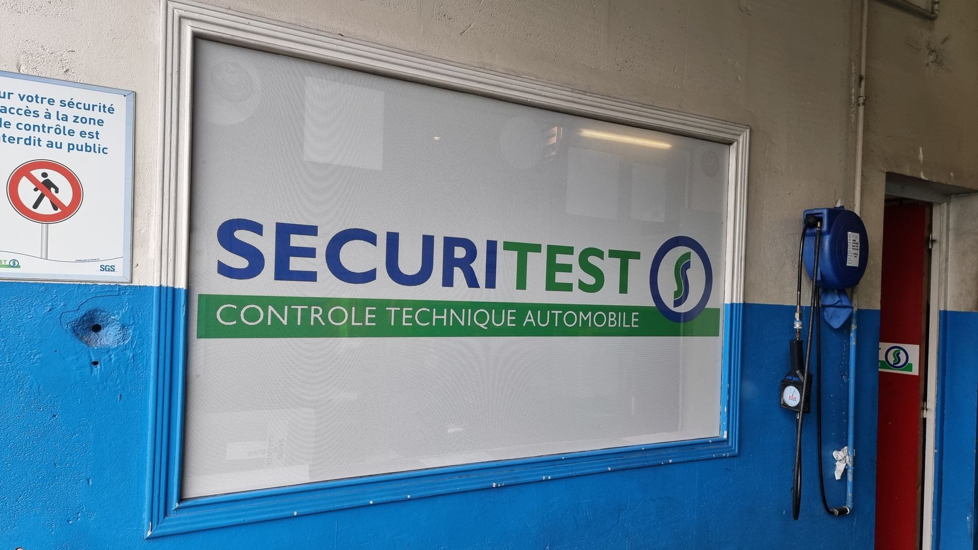 Panneau pour Securitest, un service d'inspection automobile, avec des lettres bleues et vertes sur une vitre.