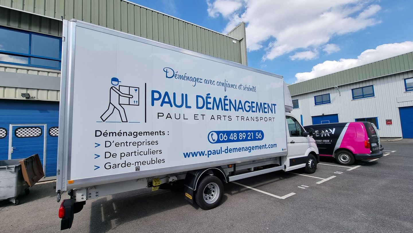 Un camion de déménagement blanc portant le logo Paul Déménagement est stationné devant un immeuble.