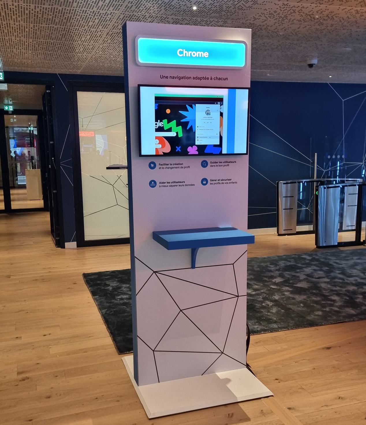 Borne Chrome OS avec un écran affichant un jeu, une étagère bleue et un motif géométrique décoratif.