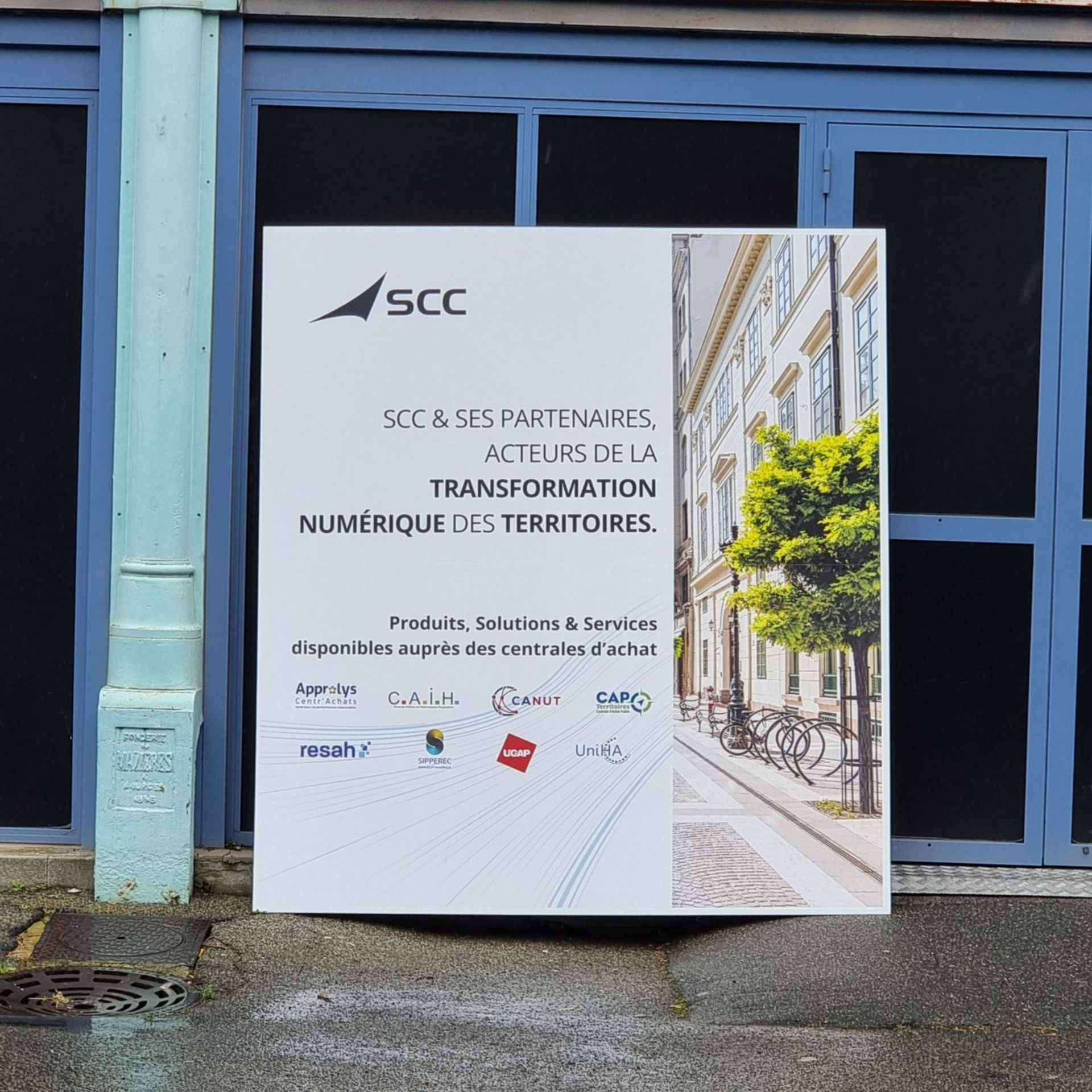 Panneau indiquant SCC, devant une porte bleue. Affiche du texte et l'image d'un bâtiment.