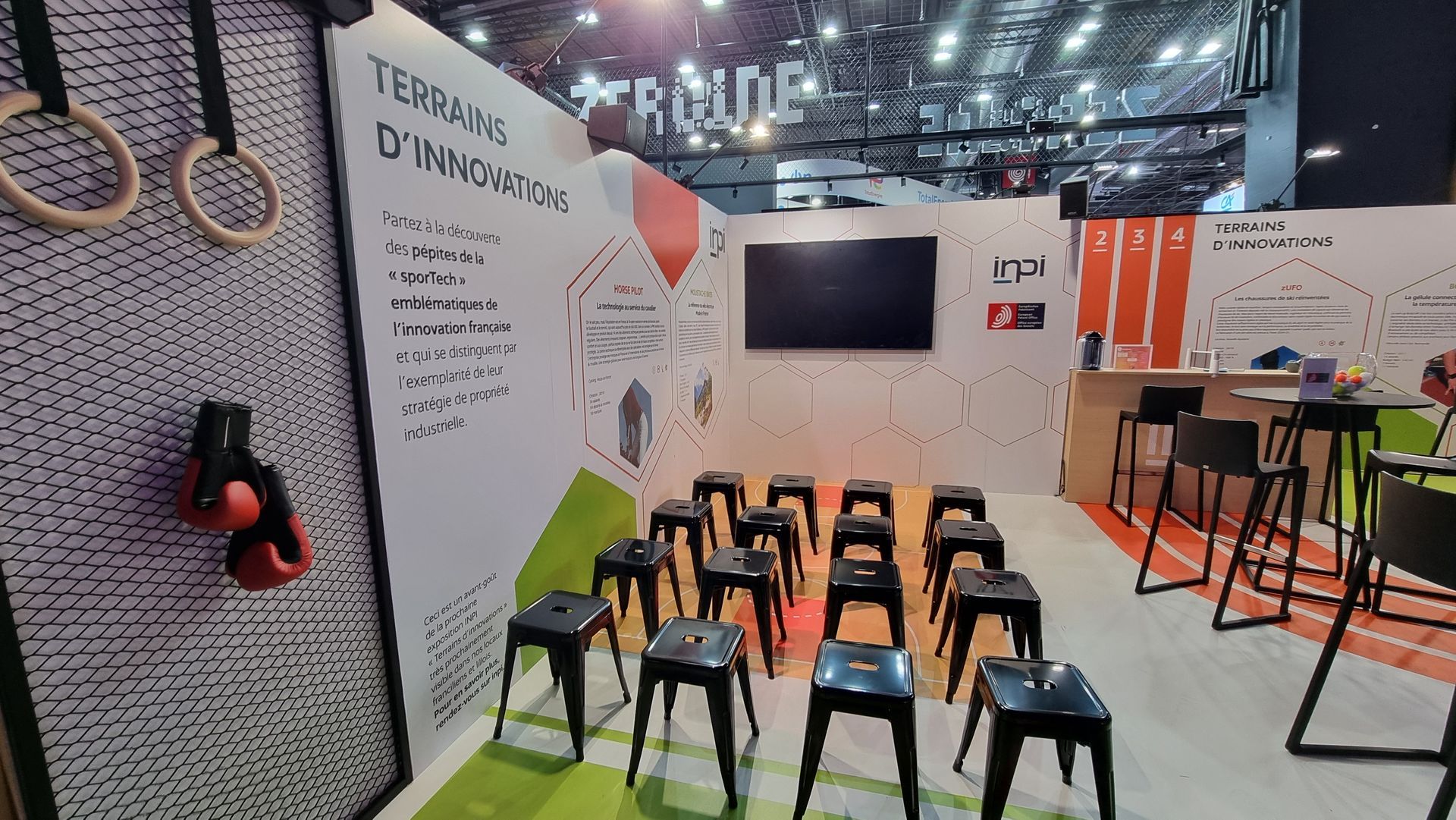 Stand d'exposition avec tabourets noirs, anneaux, gants de boxe.