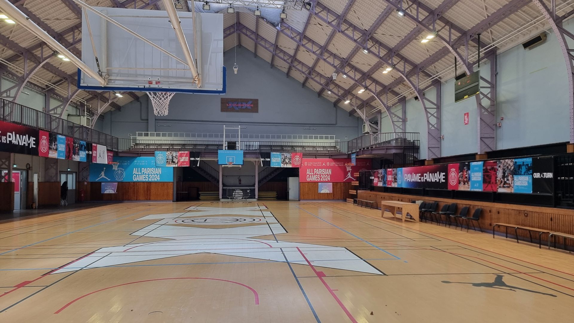 Terrain de basket-ball à l'intérieur d'un gymnase avec un haut plafond voûté ; plusieurs banderoles ornent le terrain