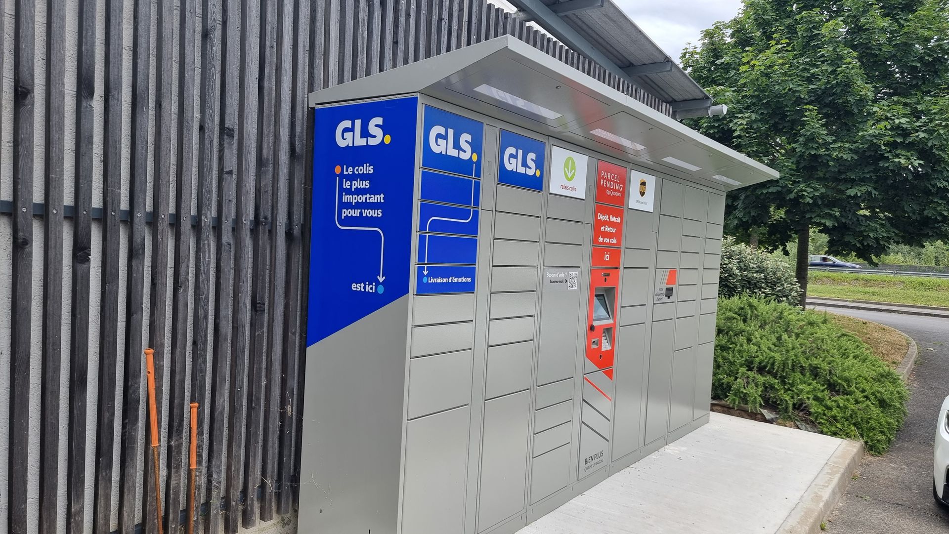 Un casier à colis GLS à l'extérieur, montrant plusieurs compartiments et des panneaux d'instructions en bleu, blanc, vert et rouge.