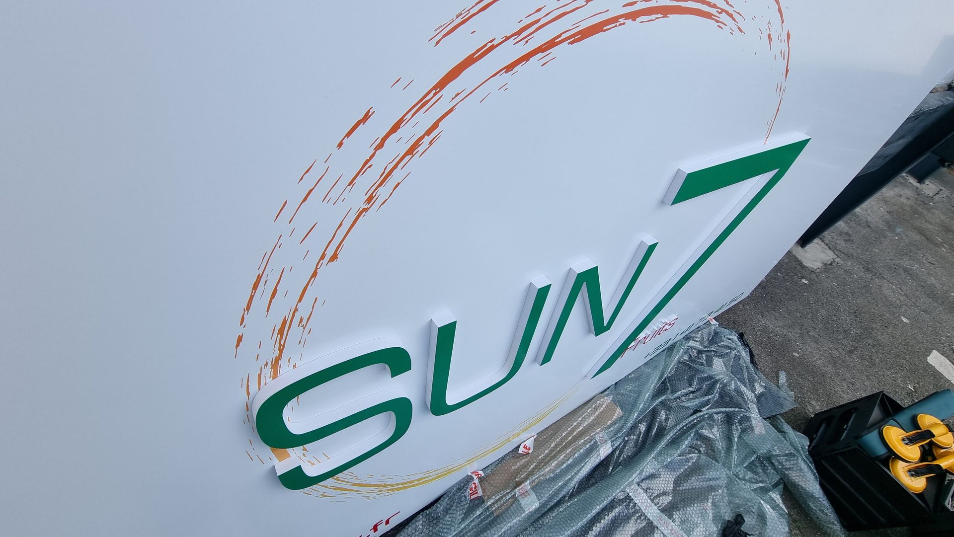 Panneau blanc avec inscription verte SUN 7, motif circulaire orange.