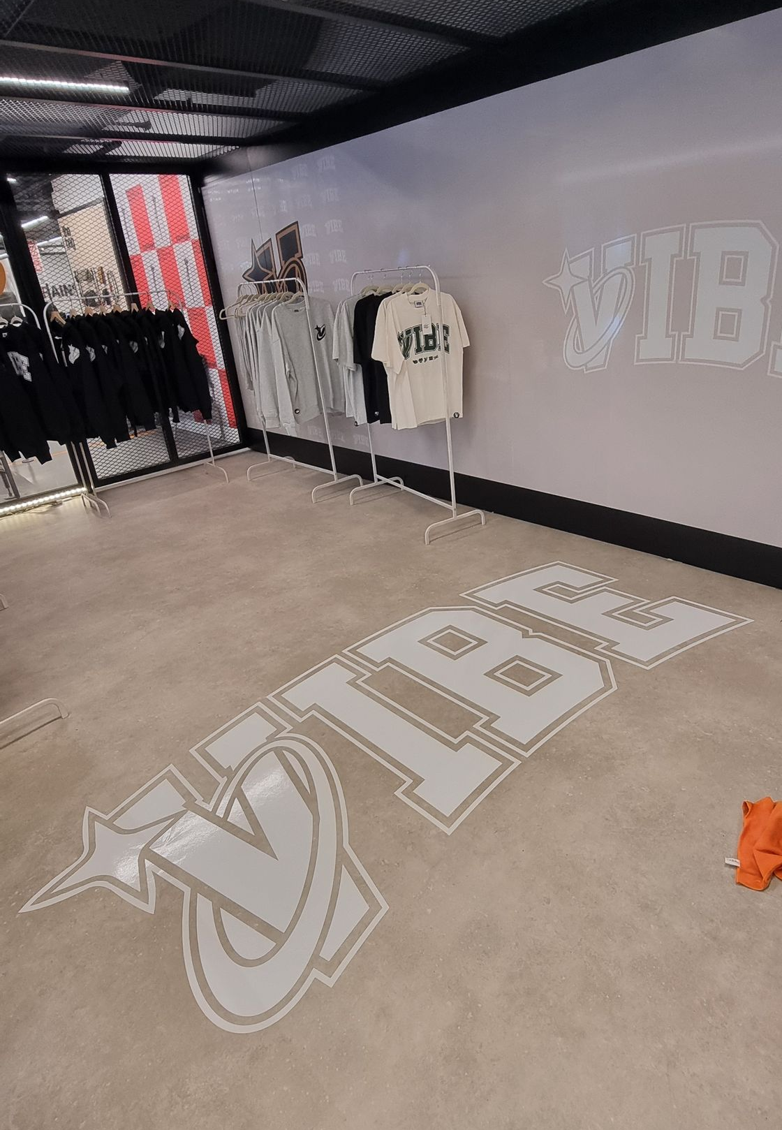 Intérieur d'un magasin de vêtements avec l'inscription « VIBE » au sol et aux murs. Portants de vêtements et plafond noir.