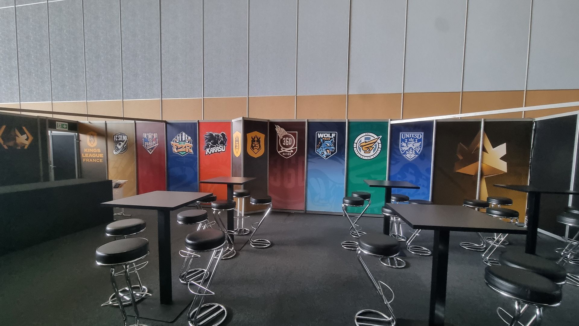 Une pièce ornée de bannières à motifs, de tables de bar avec tabourets et d'un bar noir.