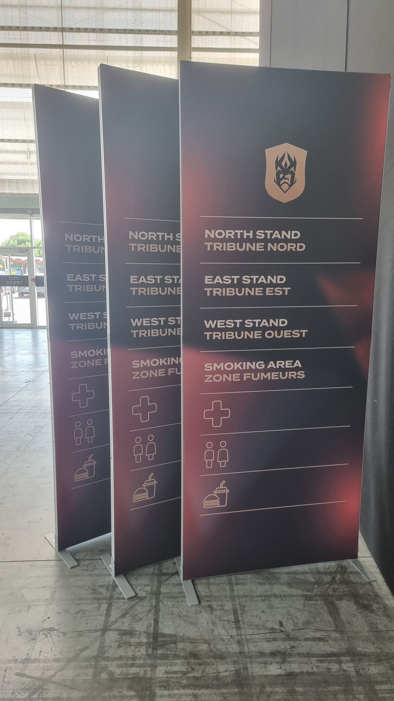 Trois grands panneaux à inscription bordeaux et or. Un blason doré en haut, des listes de mots en dessous.