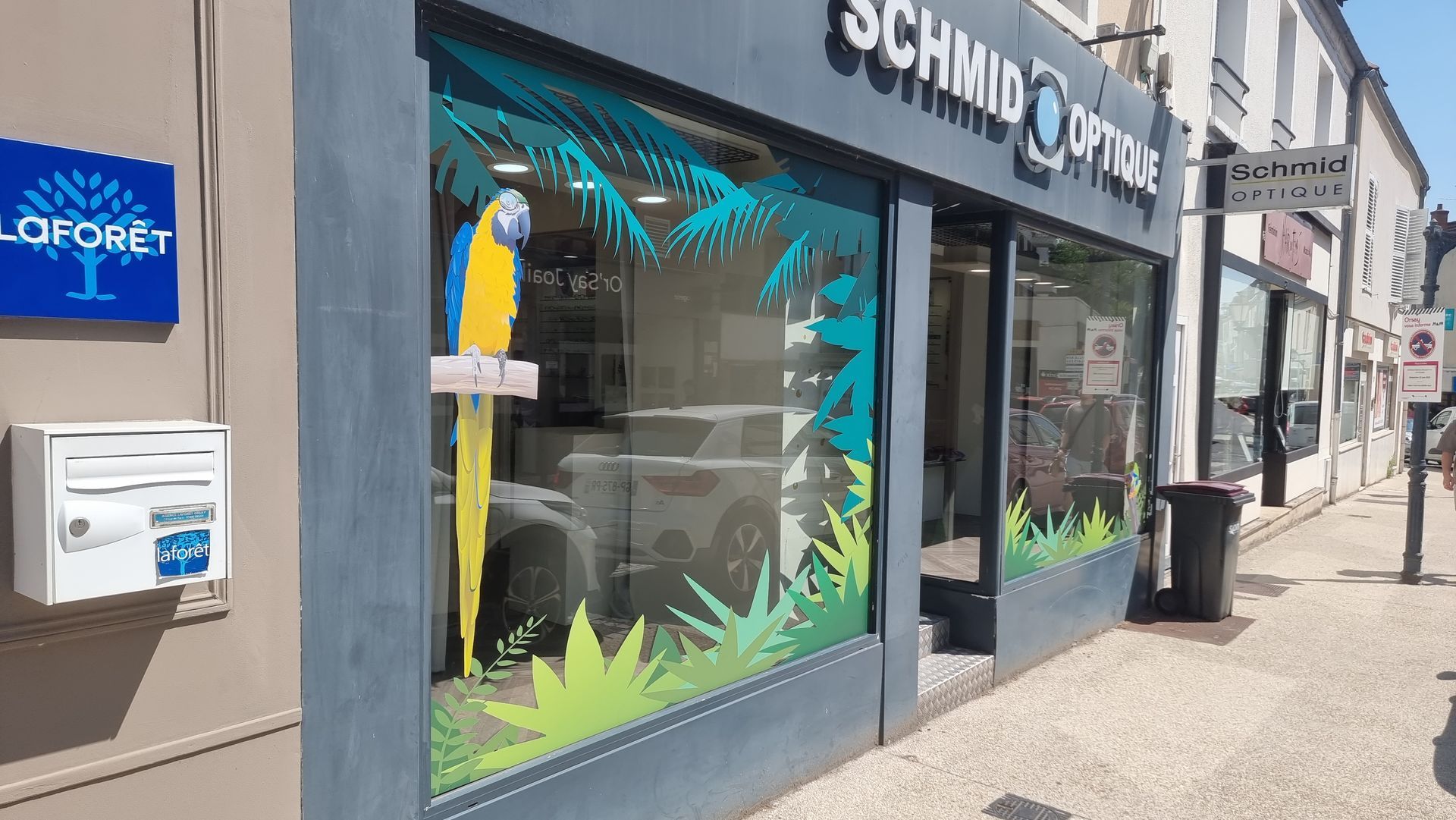 Façade du magasin Schmid Optik ornée de perroquets. Détails bleus et verts. Extérieur du bâtiment.
