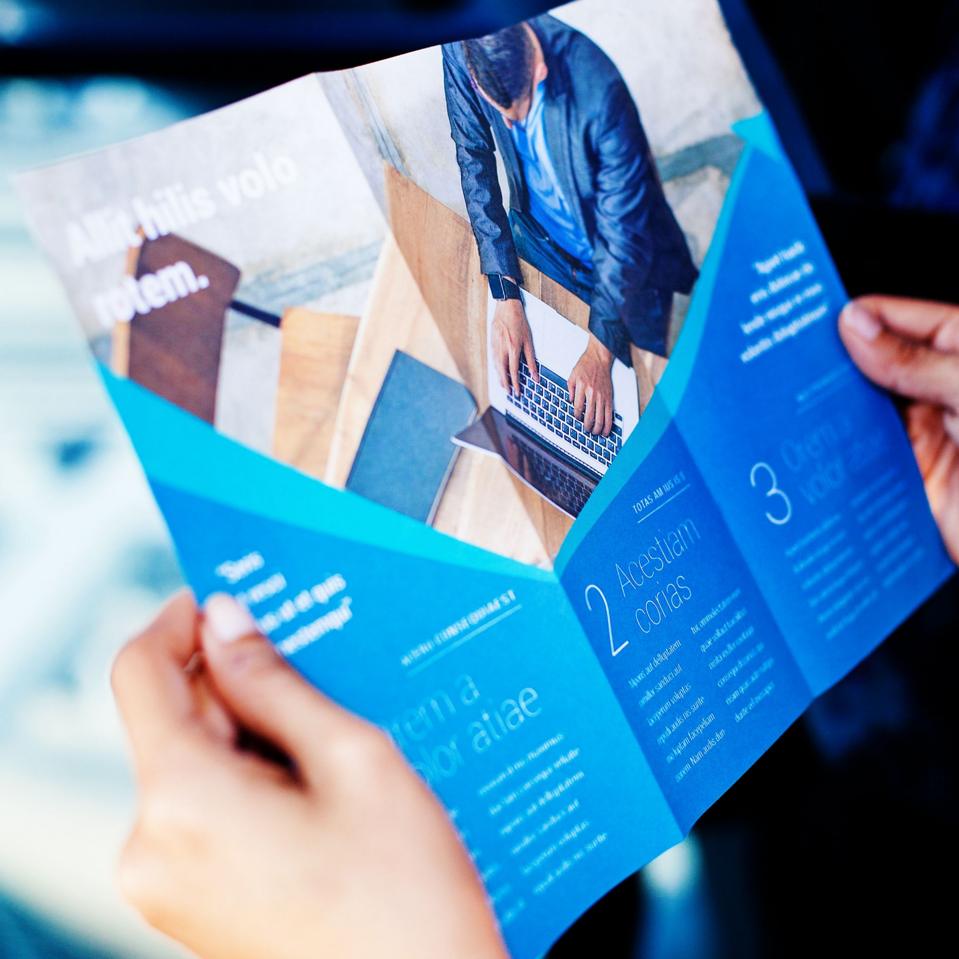 Une personne tenant une brochure bleue avec du texte et la photo d'une personne utilisant un ordinateur portable.