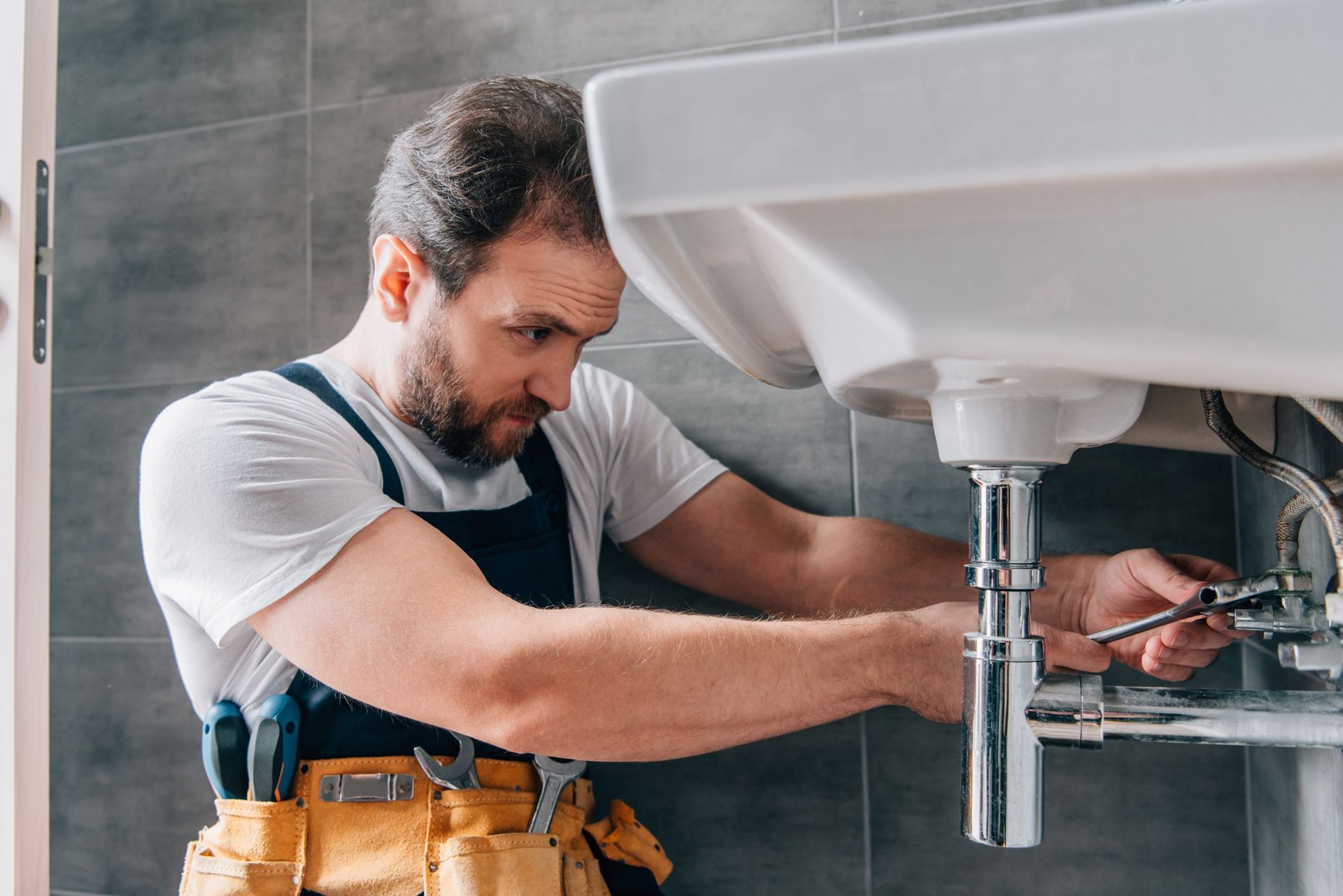 Un hombre está arreglando un lavabo en un baño con una llave inglesa.