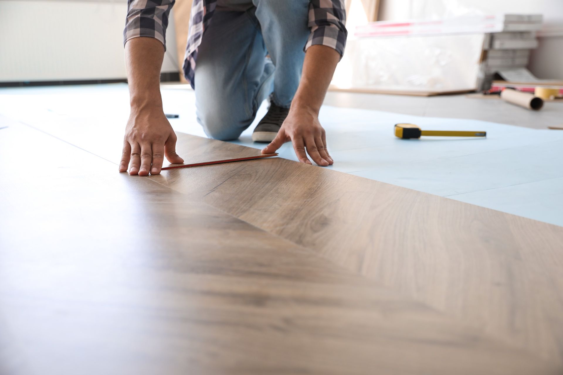 Un hombre está midiendo un piso de madera con una cinta métrica.