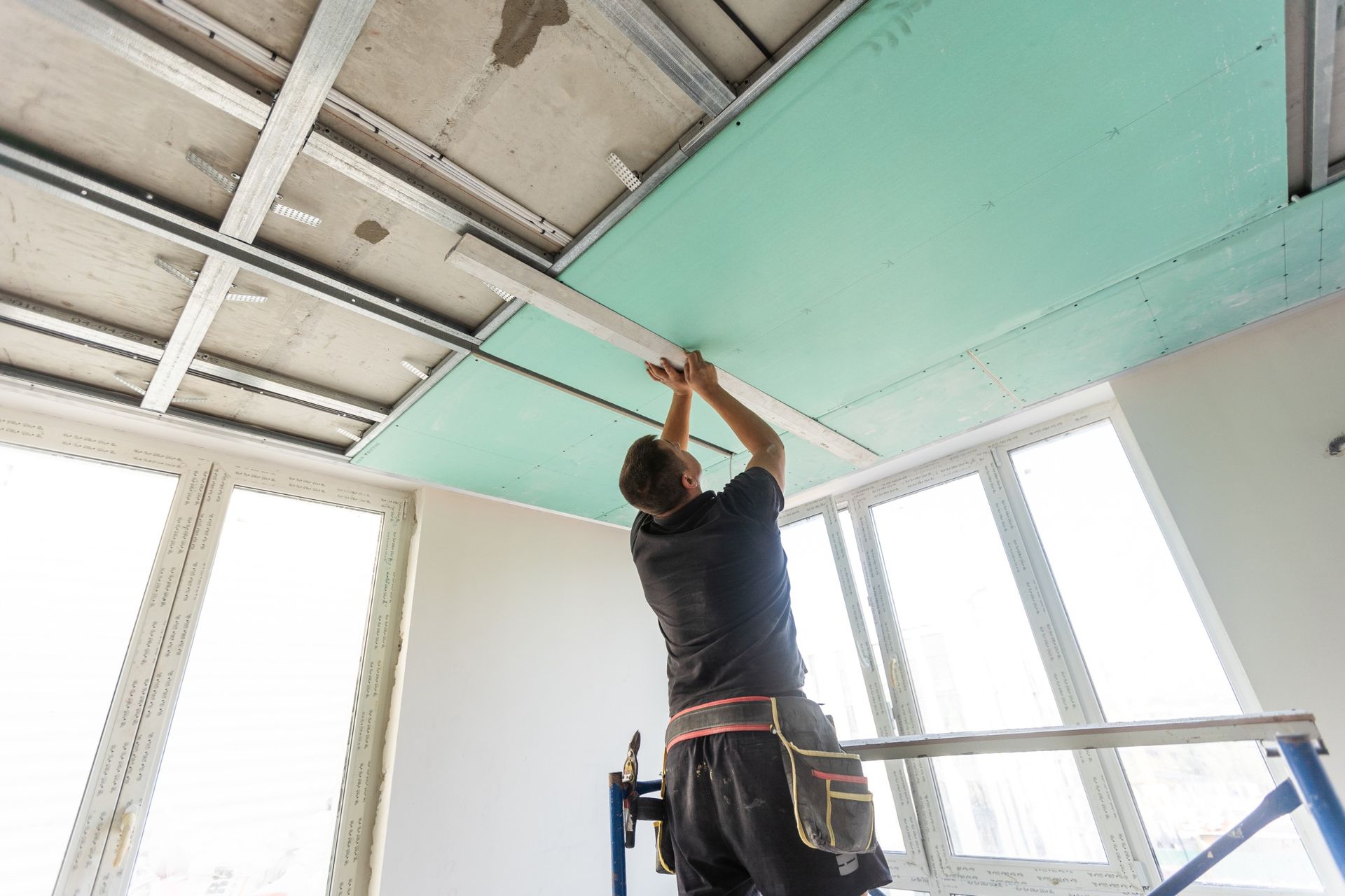 Un hombre está de pie en una escalera trabajando en un techo.