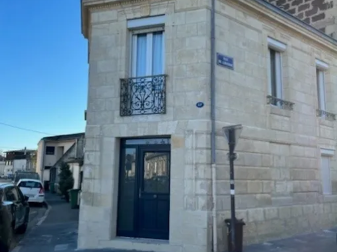 Vue d'angle d'un bâtiment en pierre couleur crème avec une porte bleu foncé, un balcon en fer forgé et un panneau de rue bleu.