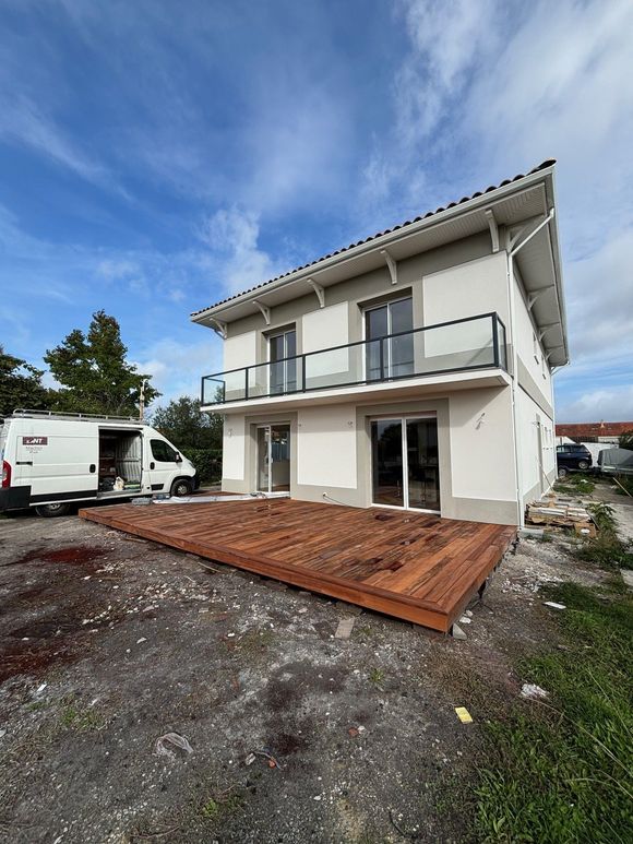 Bâtiment beige avec fenêtres et porte blanches, cyprès et marches en pierre menant à l'entrée.