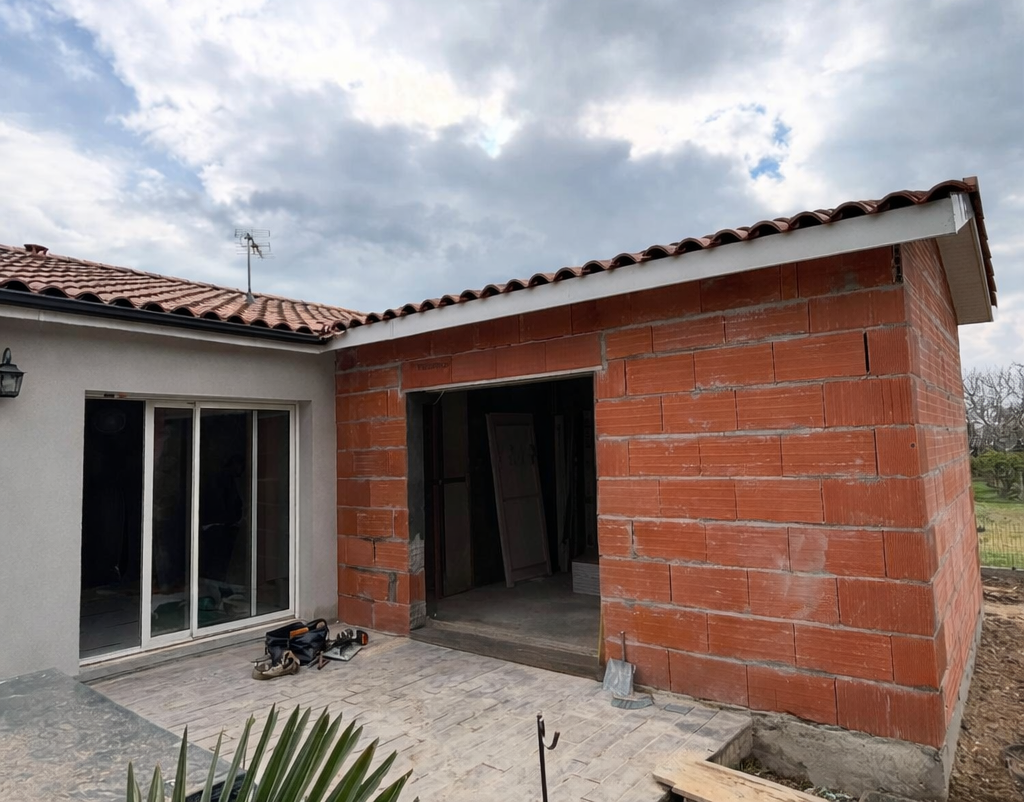 Chantier : structure en briques rouges accolée à un bâtiment avec des portes coulissantes en verre.
