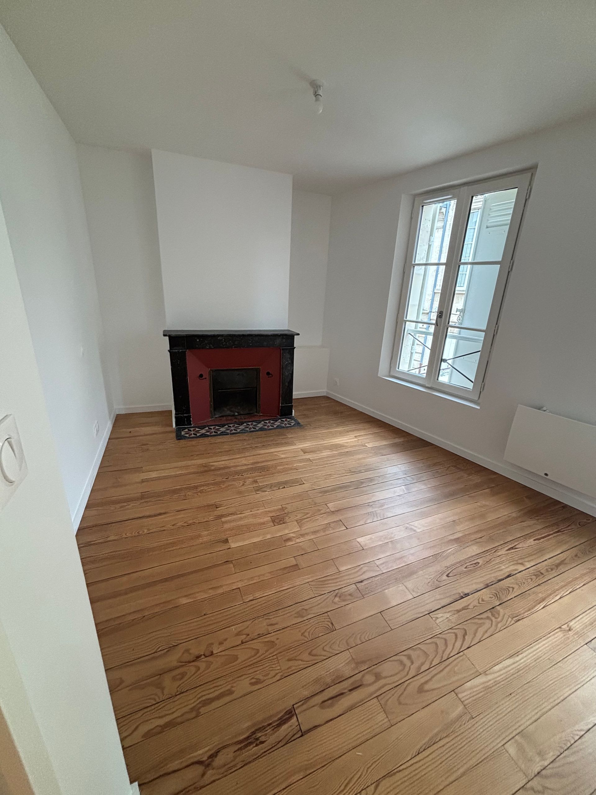 Pièce vide avec parquet clair, murs gris et blancs, mur en briques apparentes.