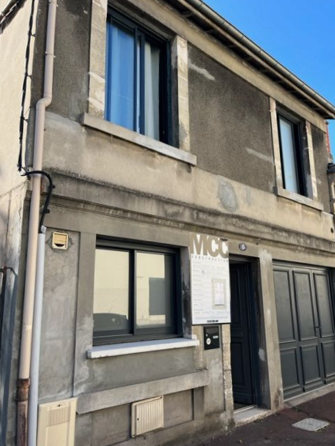 Maison blanche de plain-pied avec volets et porte marron. Allée en béton menant à l'entrée. Ciel couvert.