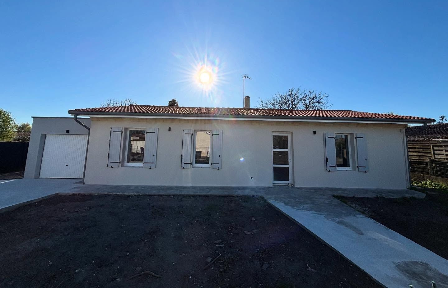 Petite maison beige aux volets blancs ; soleil éclatant au-dessus.