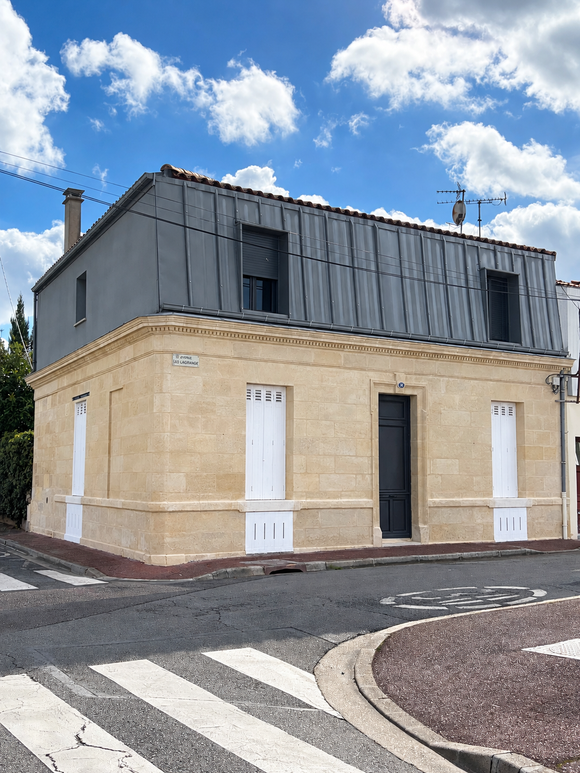 Une pelleteuse jaune creuse la terre près d'une maison blanche sous un ciel bleu et ensoleillé.