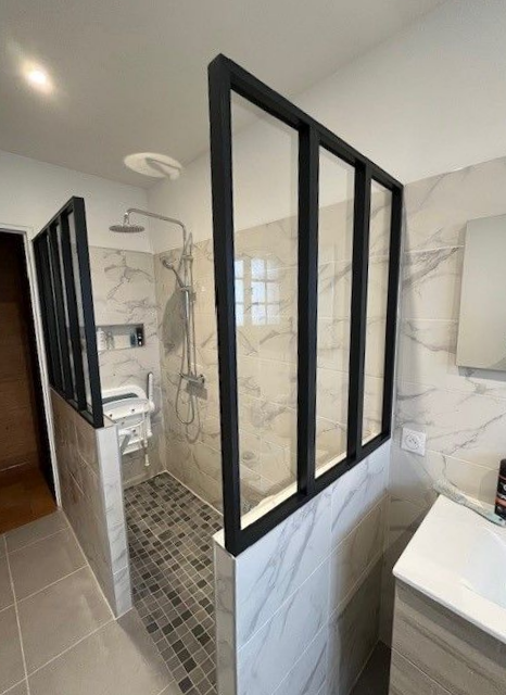 Salle de bains avec paroi de douche en verre à cadre noir, carrelage imitation marbre et siège de douche accessible.