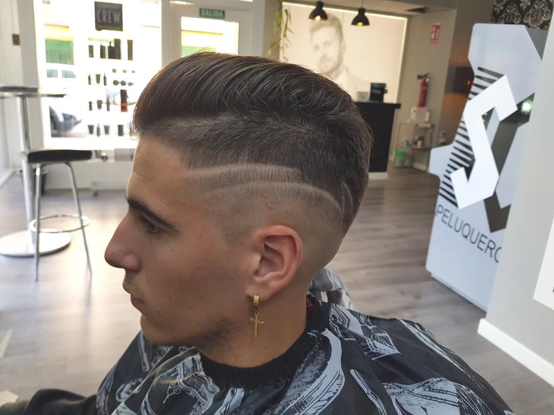 Perfil de una persona con el pelo corto y degradado, con un diseño de líneas rapadas, sentada en una peluquería.
