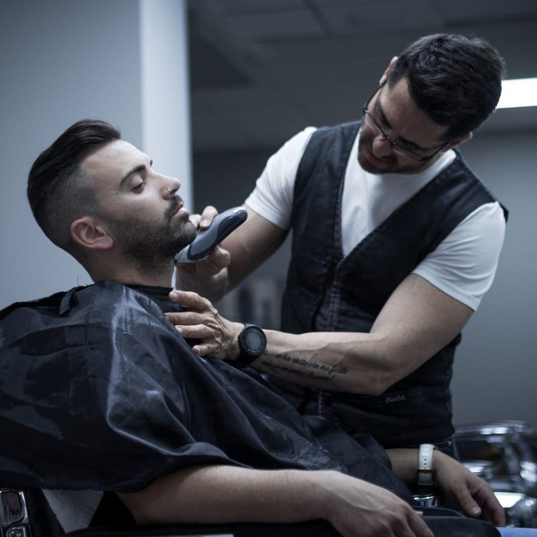 Un barbero con chaleco negro utiliza una recortadora eléctrica para arreglar la barba