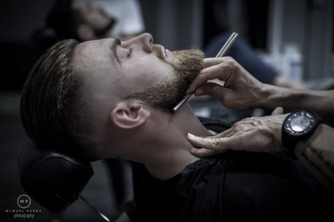 Un barbero utiliza una navaja de afeitar para afeitar la barba de un cliente en un estudio.