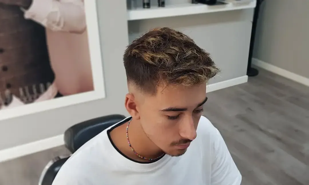Una persona con el pelo corto, texturizado y con mechas, y un rapado lateral degradado, sentada en una silla de barbero.