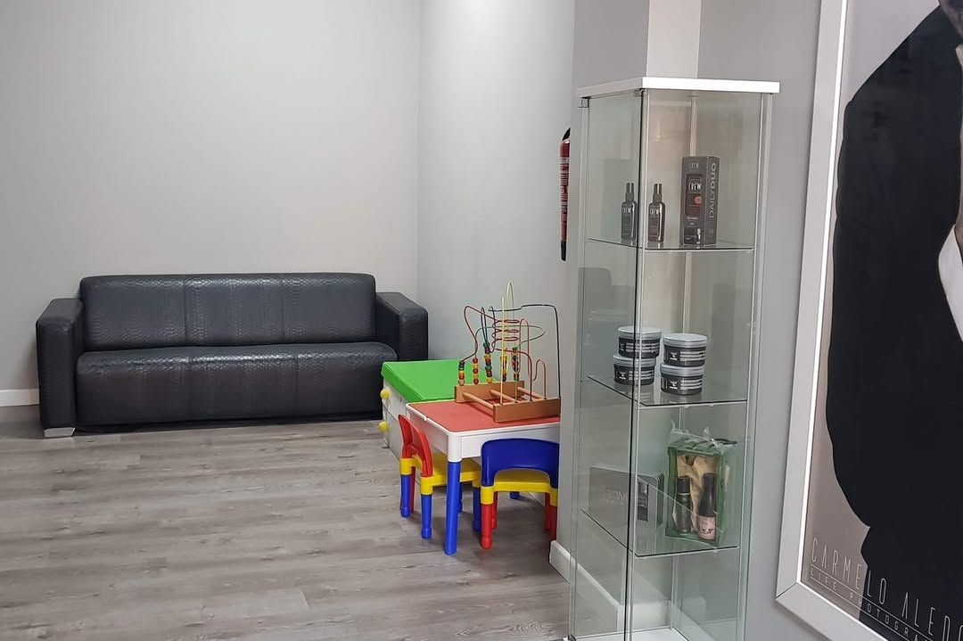 Una sala de espera con un sofá de cuero oscuro, un pequeño conjunto de mesa y sillas de colores y una vitrina de cristal.