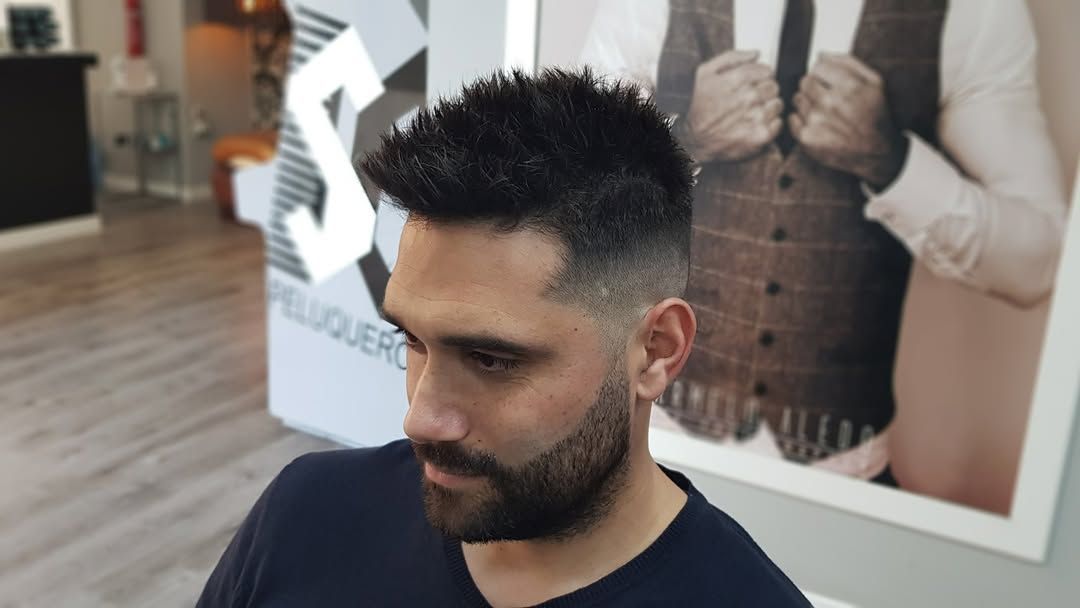 Un hombre con el pelo corto y descolorido y la barba recortada mira hacia otro lado