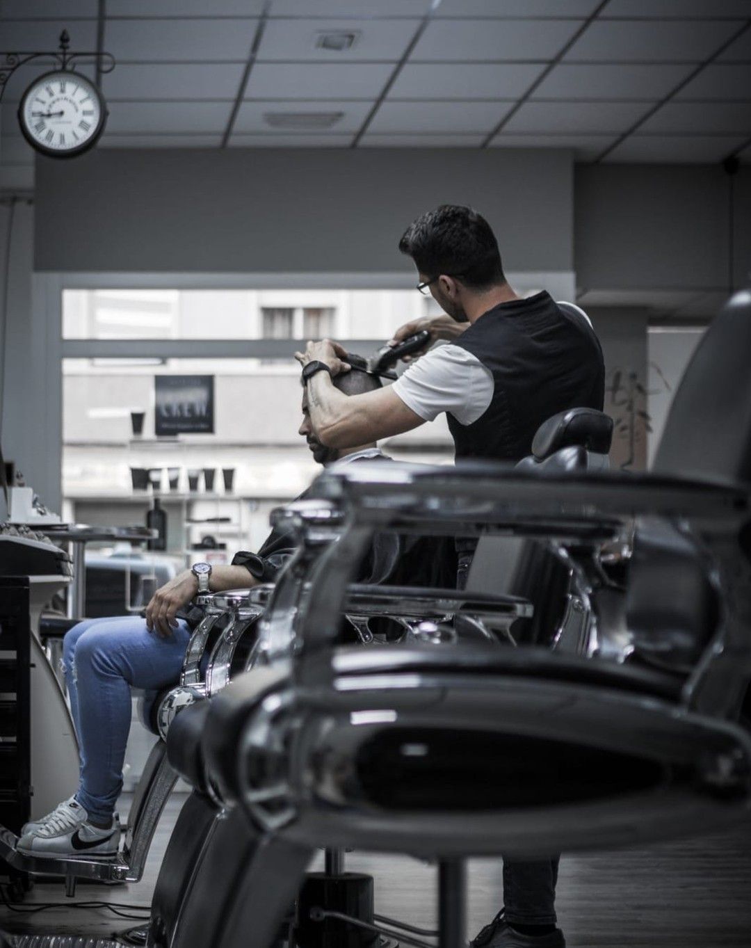 Un barbero le corta el pelo a un cliente en una peluquería, visto desde atrás