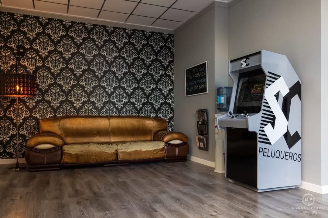 Un sofá de cuero dorado se encuentra junto a una pared con estampado de damasco, al lado de una máquina recreativa gris