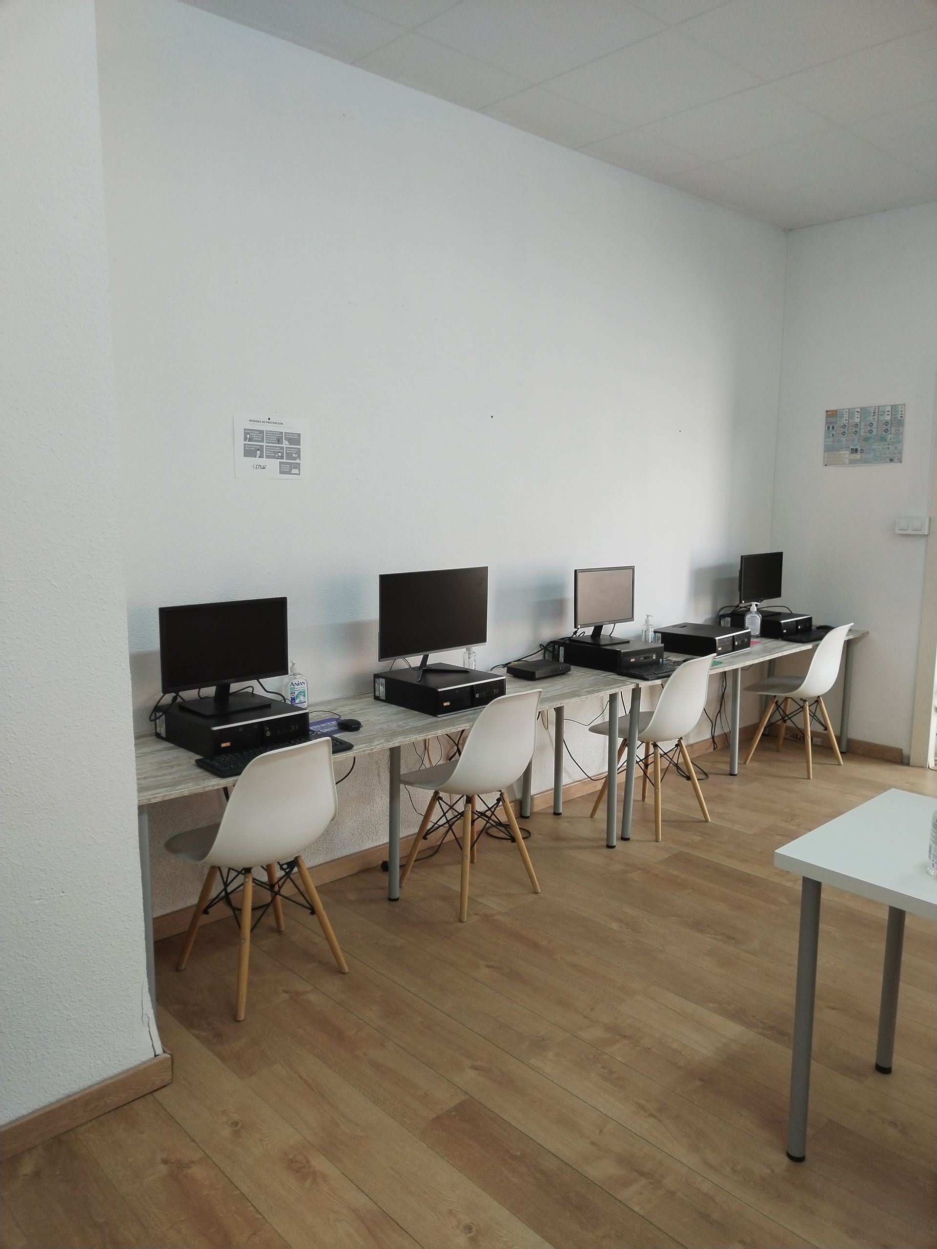 Un laboratorio de computación con cuatro estaciones de trabajo a lo largo de una pared blanca, cada una con un monitor