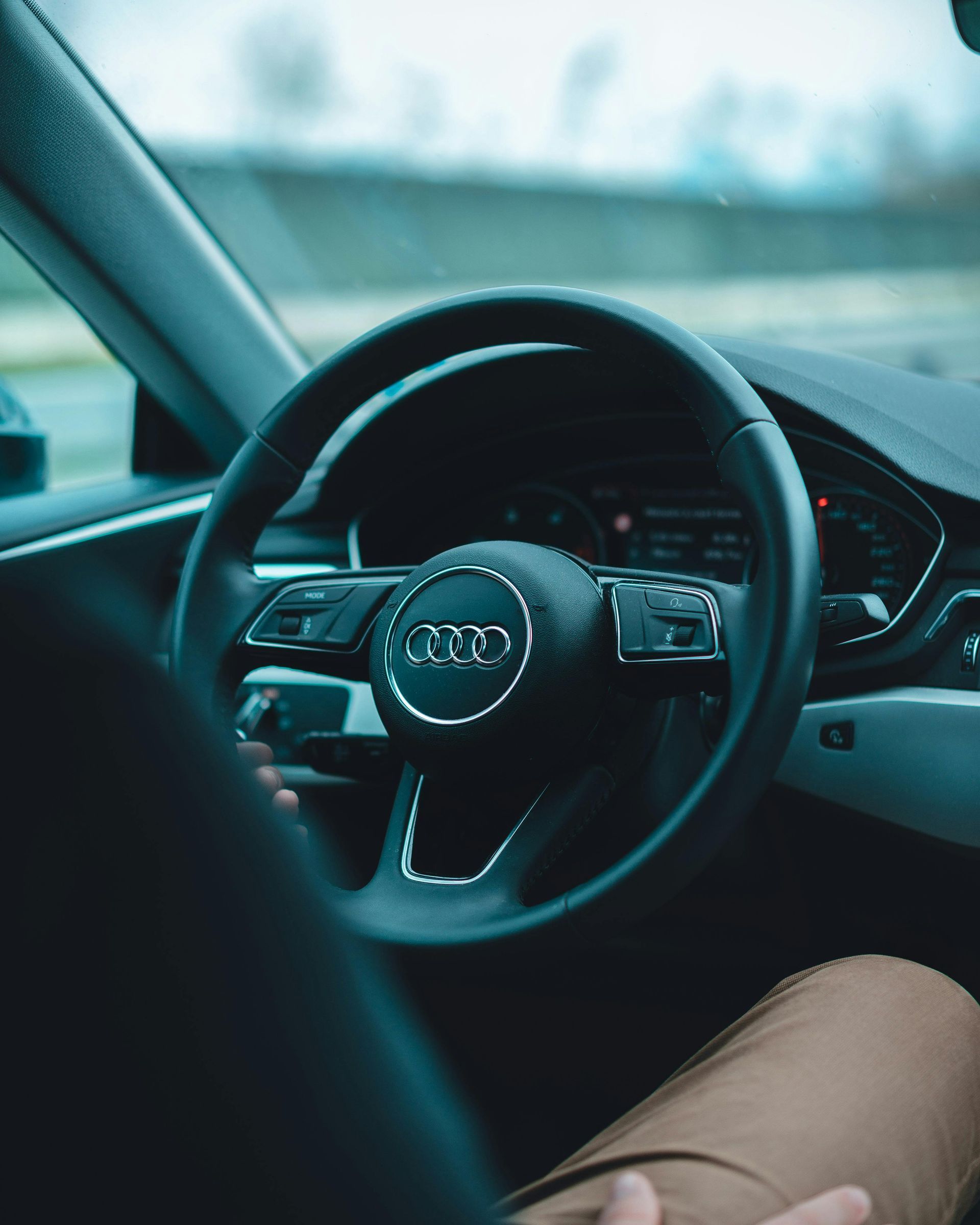 Las manos de una persona en el volante de un Audi, con el interior del coche y el tablero visibles.