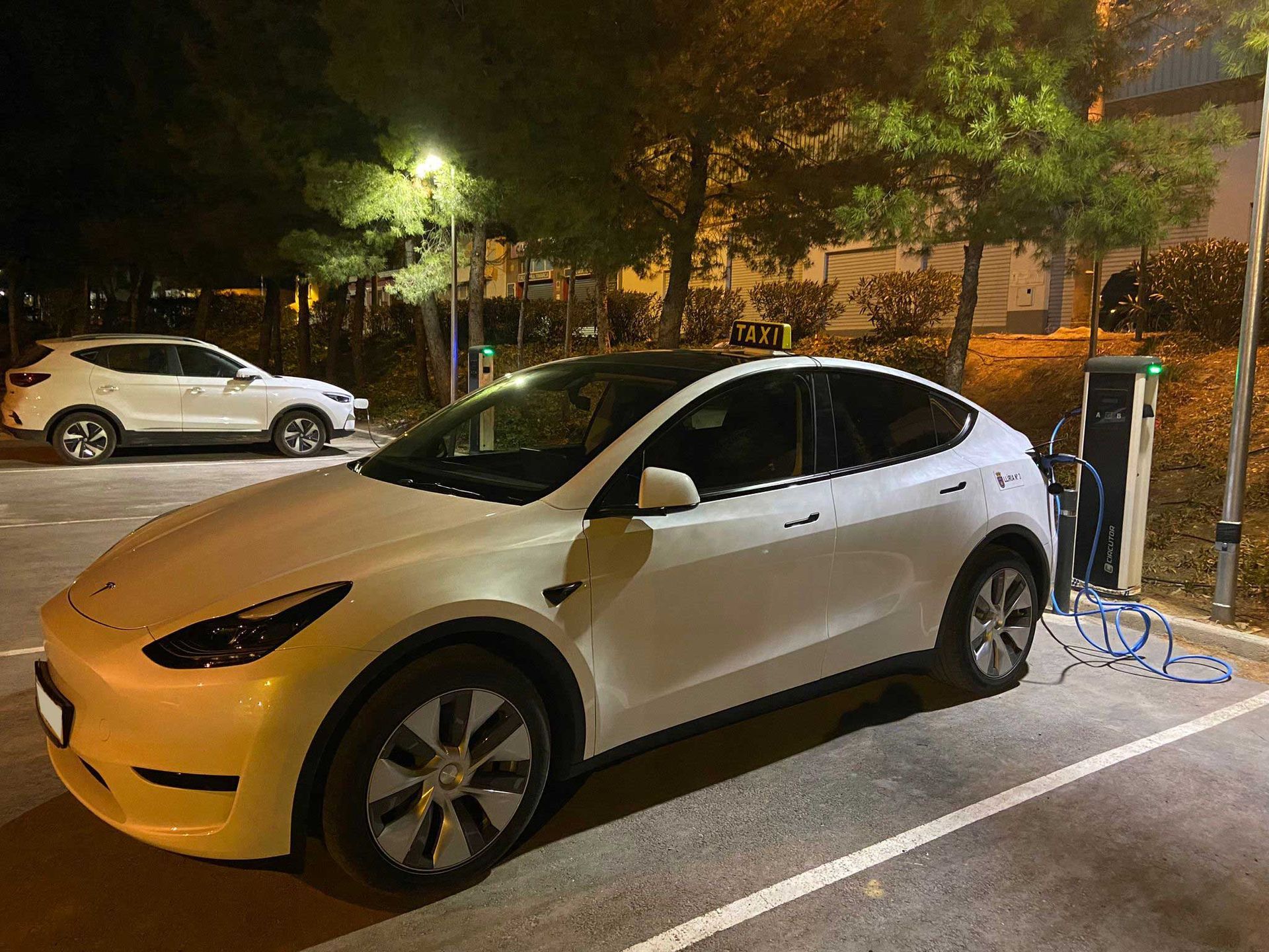 Un Tesla modelo Y blanco se está cargando en una estación de carga por la noche.
