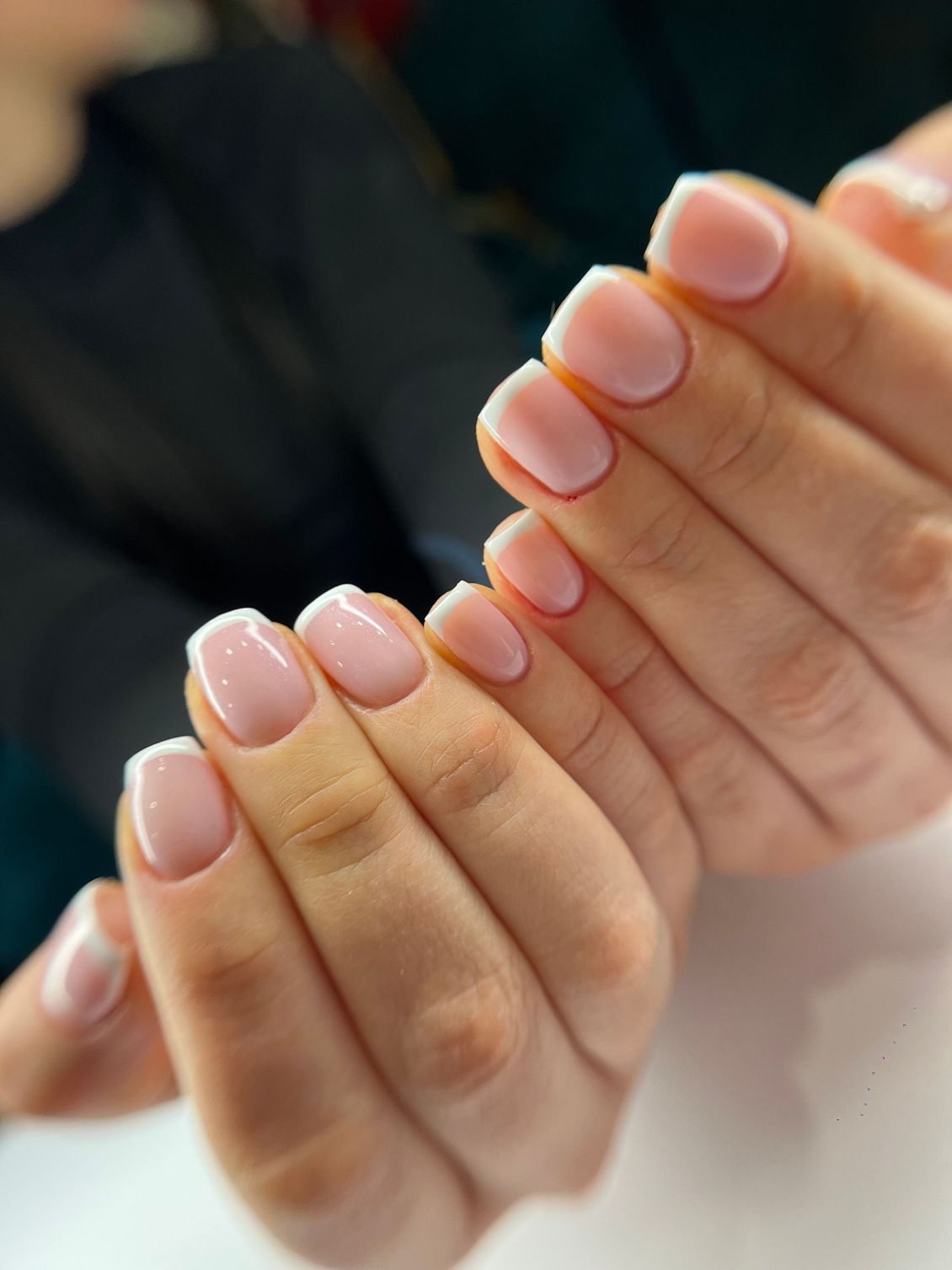 Mains avec manucure française, ongles courts et arrondis aux pointes blanches sur une base rose clair.