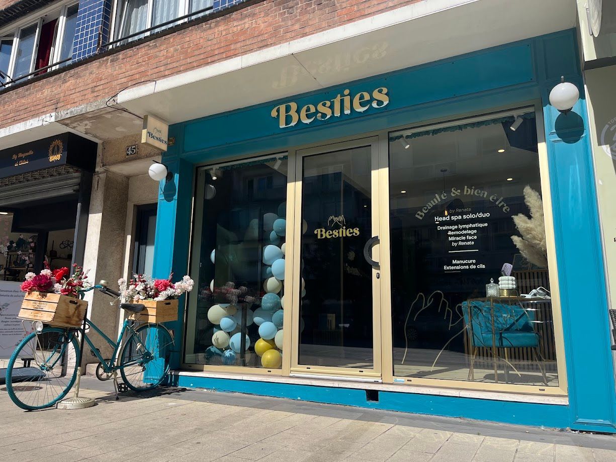 Extérieur de la boutique Besties avec une façade turquoise, des ballons et un vélo avec des paniers à fleurs.