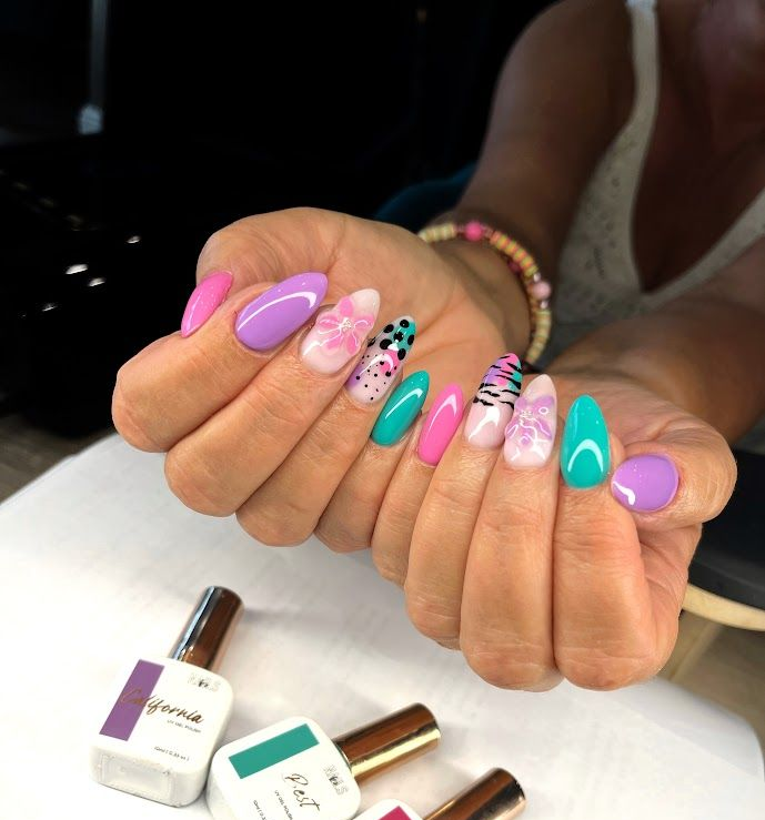 Des mains aux ongles longs, colorés et décorés. Les vernis à ongles sont notamment rose, turquoise et violet.