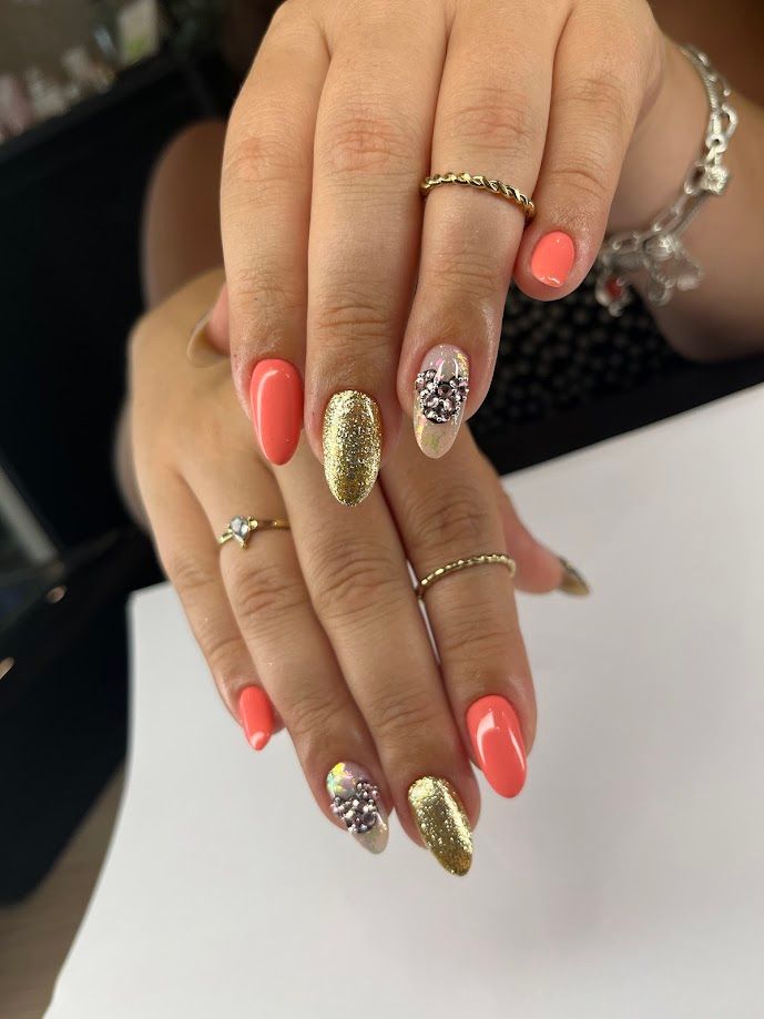 Des mains avec des ongles en gel corail et or ; certaines ornées de strass.