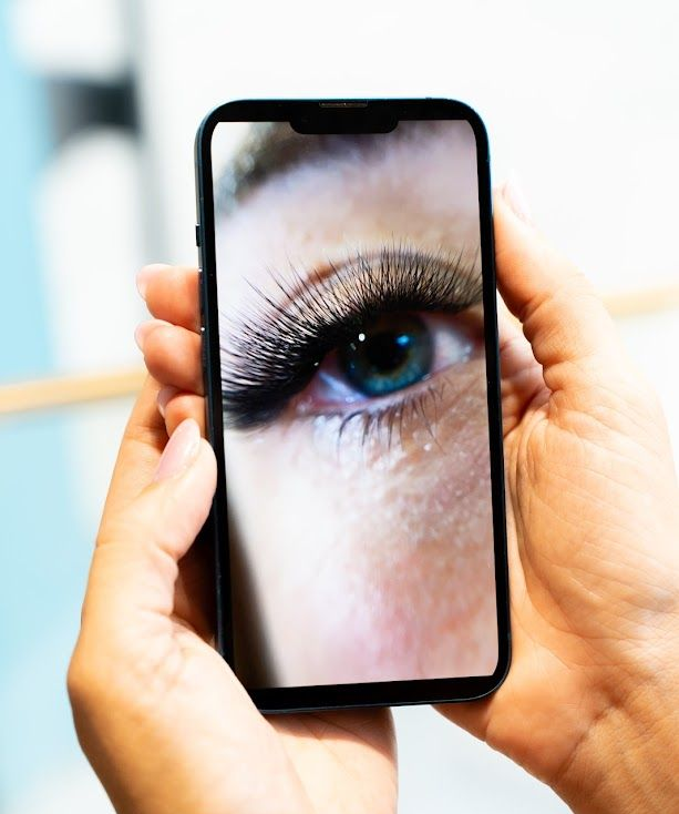 Des mains tenant un téléphone affichant un gros plan d'un œil bleu aux longs cils foncés.