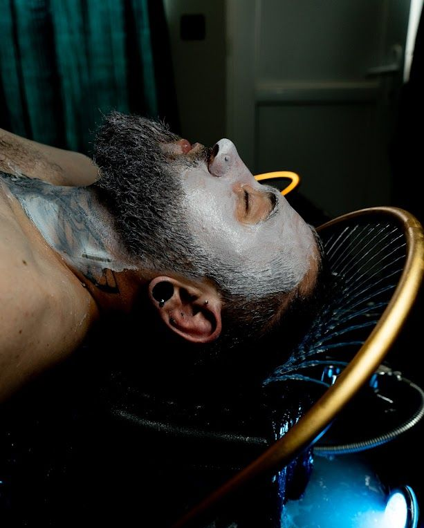 Un homme barbu, couvert d'une substance blanche, est allongé sur le dos tandis que l'eau coule. Un anneau d'or entoure sa tête.