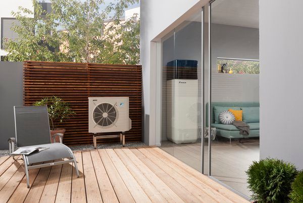 Patio moderne avec chaise longue, climatiseur extérieur, terrasse en bois et portes coulissantes en verre donnant sur un intérieur meublé